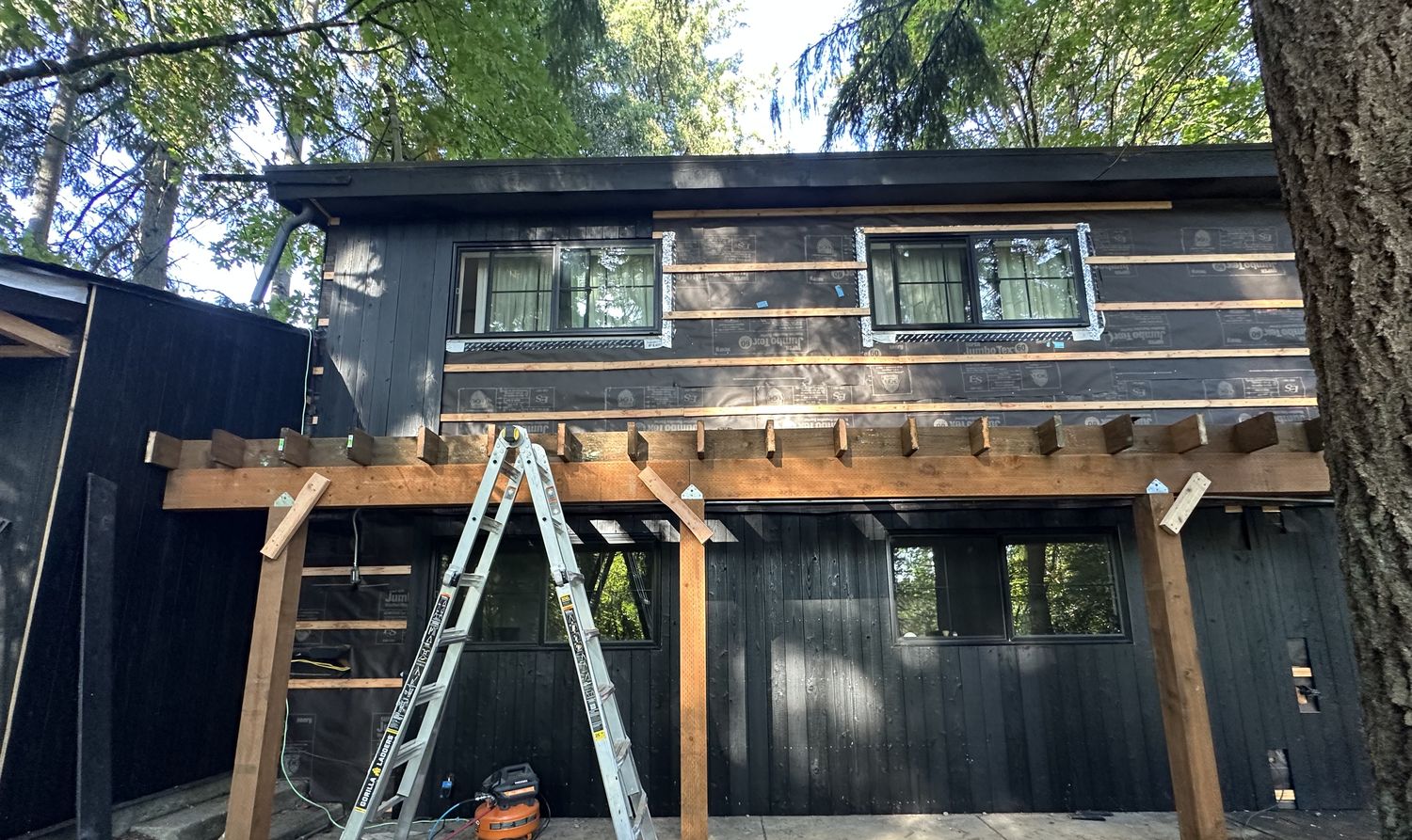 Completed heavy timber covered structure attached to a dark-stained building exterior